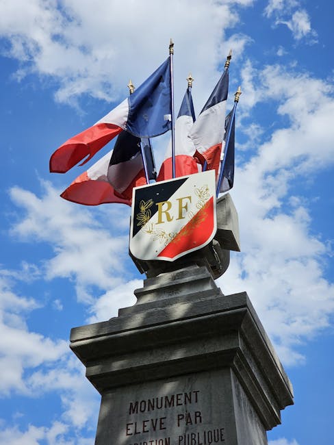 A monument in France displaying multiple flags under a clear blue sky.